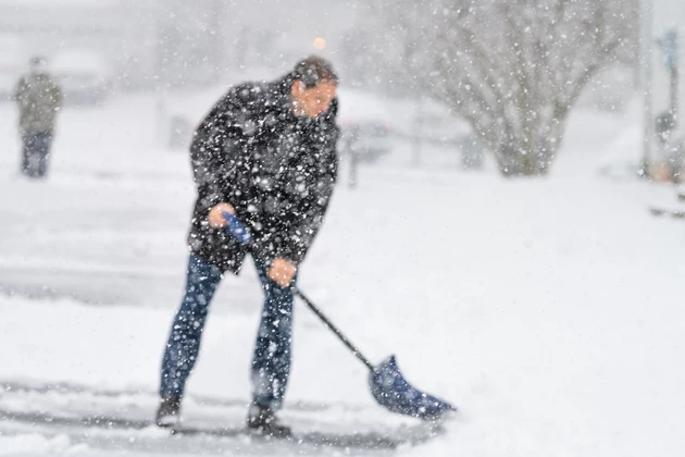 Defocused young man, male in winter coat cleaning, shoveling driveway, street from snow in heavy snowing snowstorm, holding shovel, residential houses, snowflakes falling